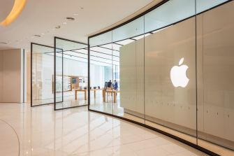Interior view of an Apple store featuring glass walls and the Apple logo prominently displayed.