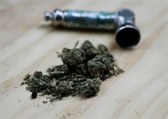 A close-up of marijuana buds and a smoking pipe on a wooden surface.