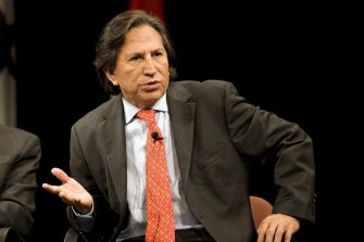 A man in formal attire speaking gesturing during a discussion or presentation.