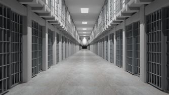 A long, empty prison hallway lined with barred cells on both sides.