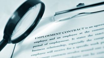 A magnifying glass and a clipboard positioned over an employment contract document, highlighting the text.