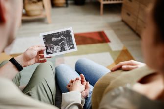 Close-up of a person holding a pregnancy ultrasound photo in a living room.