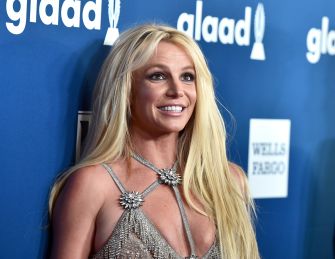 Blonde woman in a sparkling silver dress posing on a blue carpet with GLAAD signage in the background.