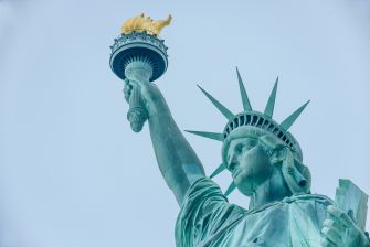 Close-up of the Statue of Liberty raising her torch against a clear blue sky.