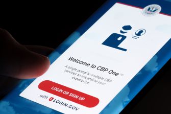 Close-up of a finger on a smartphone screen displaying the CBP One app login page with the "Welcome to CBP One" header.