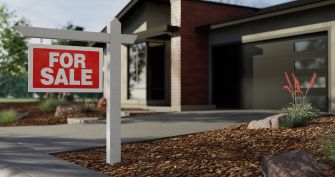 A "For Sale" sign in front of a house, indicating it's available for sale.