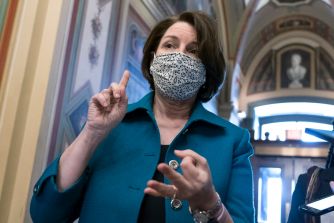 Senator Amy Klobuchar gestures while discussing antitrust legislation, wearing a mask in a legislative setting.