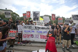 A crowd of protesters holding signs demanding justice for Alton Sterling and opposing police brutality during a Black Lives Matter demonstration.