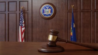 Wooden gavel on a judge’s bench in a courtroom, with a U.S. flag and a state seal in the background.