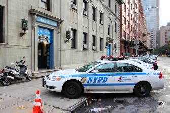 NYPD police car parked on a city street with tall buildings and an orange traffic cone nearby