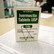 A box of Ivermectin tablets on a pharmacy counter, with prescription paperwork in the background.