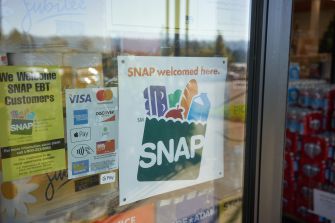 Storefront window with SNAP signs, including a large “SNAP welcomed here” poster and payment logos (Visa, Mastercard, American Express, Discover, Apple Pay, Google Pay), plus a yellow “We Welcome SNAP EBT Customers” sign.