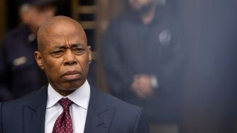 New York City Mayor Eric Adams addressing the media, with a serious expression, amidst ongoing legal challenges.