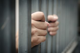 Close-up of hands gripping prison bars, symbolizing confinement and legal issues.