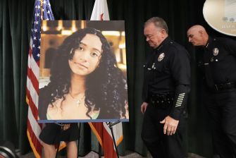 Two police officers stand beside a large portrait of Celeste Rivas Hernandez at a press event, with American flags in the background.