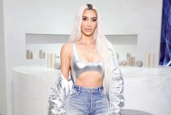Kim Kardashian poses in a silver outfit with a minimalist background.