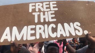 A crowd holding a sign that reads "FREE THE AMERICANS."