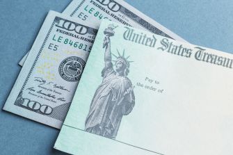 A close-up image of U.S. Treasury checks and two $100 bills on a blue background.