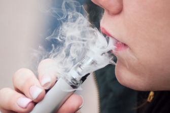 A close-up of a person vaping, exhaling vapor from an e-cigarette.