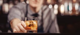 A bartender serving a drink at a bar, with blurred background elements suggesting a lively bar atmosphere.