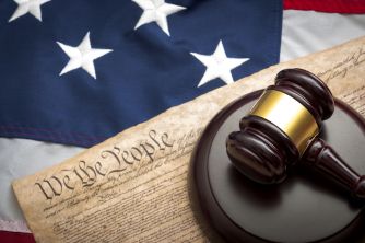 A gavel resting on a document with the words "We the People," set against an American flag background.