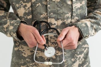 Close-up of a service member in camouflage uniform holding a stethoscope.