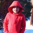 A young boy wearing a red hoodie standing outdoors in a snowy landscape.
