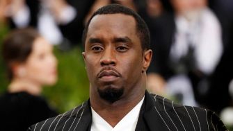 Image of a man wearing a black and white striped suit, looking serious at a public event.