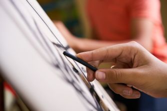 A person's hand drawing on a canvas with charcoal.