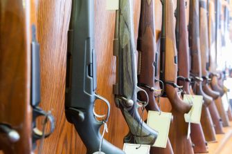 A display of various rifles mounted on a wooden wall, each with a price tag attached.