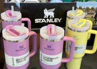 A display of colorful Stanley Quencher tumblers in various sizes, with a logo prominently featured in the background.