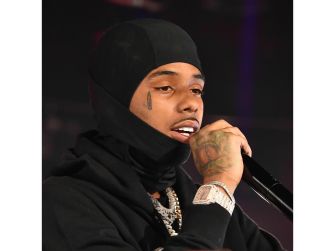 Close-up of a male rapper wearing a black durag and diamond jewelry, speaking into a microphone.