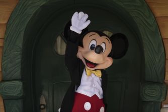 A character in a tuxedo waving, resembling a popular cartoon mouse.