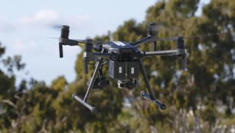 A police drone in flight against a backdrop of trees.