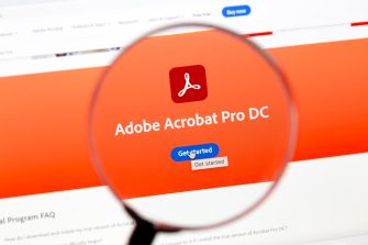 Close-up of a computer screen displaying the Adobe Acrobat Pro DC page, with a magnifying glass over the screen highlighting the Adobe logo and the text “Adobe Acrobat Pro DC.”
