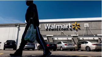 A person walking in front of a Walmart store exterior with a parking lot in view.