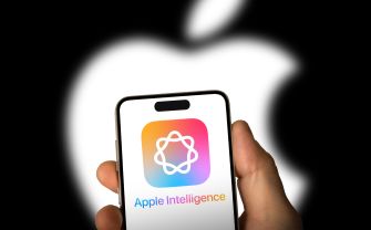 A person holding a smartphone displaying the "Apple Intelligence" app icon against a blurred Apple logo background.