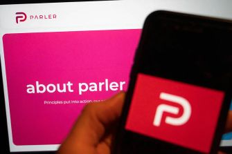 Logo of Parler displayed on a smartphone in front of a computer screen showing information about the platform.
