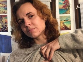 A woman in a gray sweater lifting her shirt to show scarring, expressing her experience with a double mastectomy.