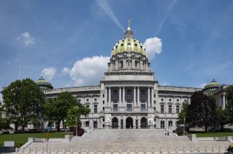 The Pennsylvania State Capitol building, an architectural landmark with a golden-domed roof, surrounded by trees and blue skies.