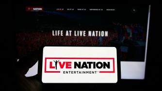 A hand holds a smartphone displaying the Live Nation logo in front of a large screen reading LIFE AT LIVE NATION, with a crowd in the background.