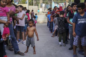 A crowd of people, including children, waiting in line in an outdoor setting.