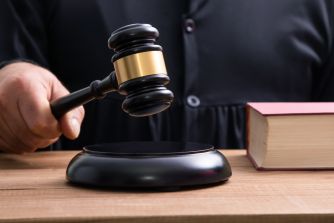 Close-up of a judge's gavel about to strike a sound block on a wooden table, with a law book nearby.