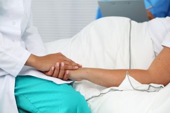 A medical professional holds the hand of a patient in a hospital setting, emphasizing the compassionate care provided in emergency situations.