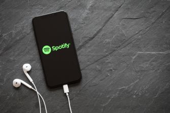 Smartphone displaying the Spotify logo on a dark slate surface with white earphones resting beside it.