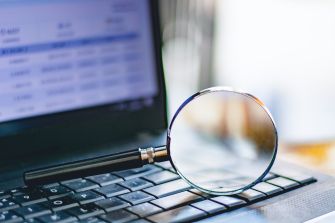 A magnifying glass on a laptop keyboard, symbolizing online searches for personal information.