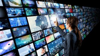 A woman pointing at a digital wall of various screens displaying images and data related to entertainment and technology.