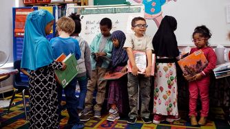 A group of diverse young students in a classroom, holding books and engaging in activities related to learning.