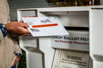 A person depositing a mail-in ballot into a drop box designated for official ballots.