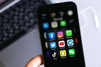 A smartphone displaying various social media app icons, including Facebook, Instagram, WhatsApp, and others, arranged in a folder labeled "Social."